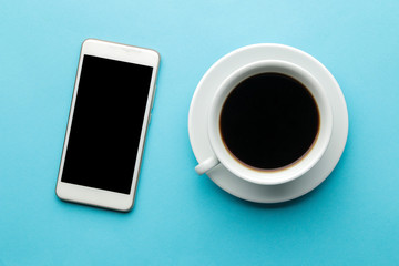 Fototapeta na wymiar Smartphone. White phone and a cup of coffee on a bright light blue background. top view.