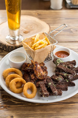 assorted snacks like chicken wings, french fries, rye bread crouton and glass of beer on wooden table
