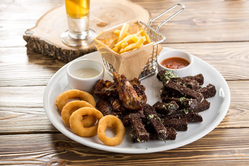 assorted snacks like chicken wings, french fries, rye bread crouton and glass of beer on wooden table