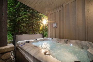 A outdoor hot tub near a forest with a sunburst coming through the trees.