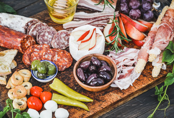 Italian appetizer on wooden board, wine snack set, salami, ham, olives, bread sticks, pickled vegetables.