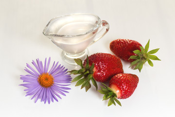 Still-life with ripe, juicy, red strawberries, cream in a glass creamer, a lilac flower on a white background. Close-up. Isolated.
