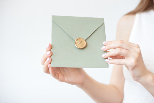 Close-up photo of female hands holding a olive invitation envelope with a wax seal, a gift certificate, a postcard, a wedding invitation card