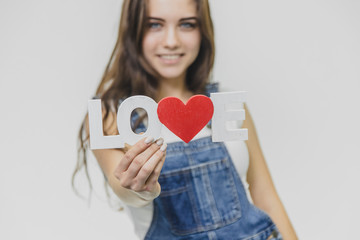 A young beautiful girl is on a gray background. Dressed in a denim suit and a white T-shirt. Holds a sign with a word of love. Opening his blue eyes smiles genuinely.