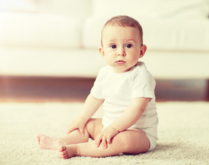 childhood, babyhood and people concept - happy little baby boy or girl sitting on floor at home