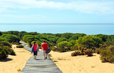 Gente en un sendero de madera entre pinos en el Paraje Natural Cuesta Maneli dentro del Parque Nacional de Doñana en la provincia de Huelva, Andalucía, España