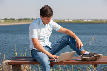 Happy man sitting on bench and using laptop in a park.