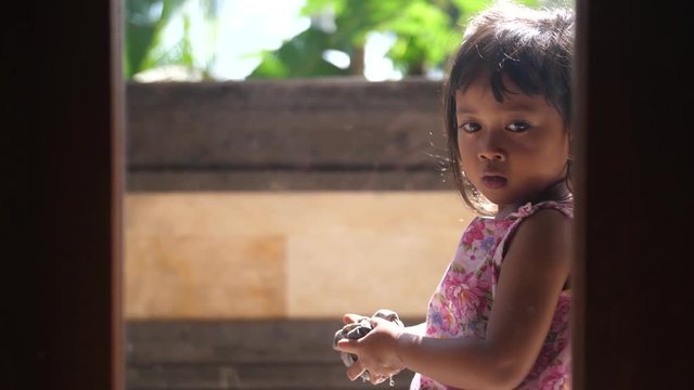Little girl doing chores wrings water from a rag used to wipe windows clean smiles for the camera. Sweet looking Balinese child working around the house helping her parents.