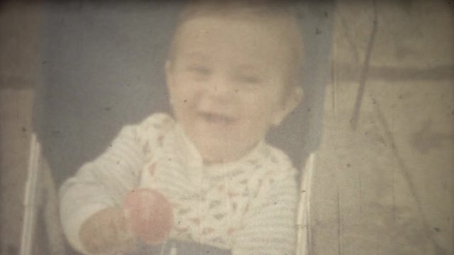 Family chronicle: Infant sitting in Baby Stroller. Father take pictures on 8mm retro cinema camera.