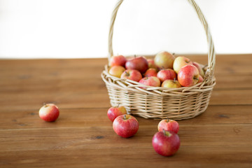 fruits, food and harvest concept - ripe apples in wicker basket on wooden table