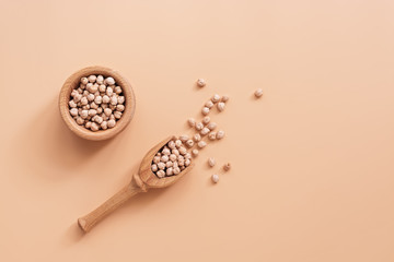Raw chickpeas in a wooden bowl and scoop on a pastel pink or peach color background. Top view, flat lay, copy space.