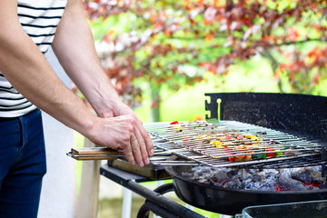 Close-up of man's hands grilling chicken breast and vegetables on a plancha in green garden. Summer barbecue party concept at home. Lockdown joys.