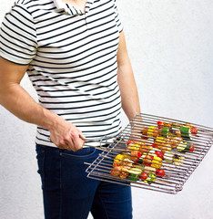 Handsome male preparing meat and vegetable-meat skewers on barbecue outdoor, enjoing cooking. BBQ summer friends party concept.