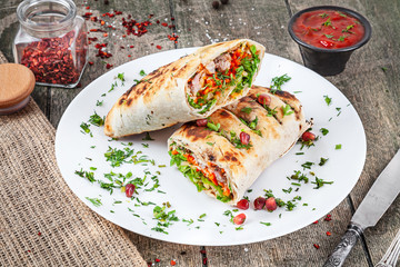 Shaurma, shawerma, kebab served on white plate with sauce. Vegan food with falafel. Arab or East cuisine. Copy space, selective focus. Shaurma with spices, cherry tomato and bell pepper