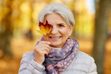 old age, retirement and season concept - portrait of happy senior woman with maple leaf at autumn park