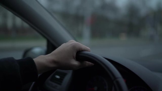 Man is traveling by car in the evening, hand on a steering wheel. Close up