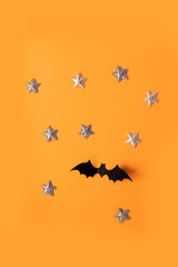 Halloween holiday concept of black paper bats fly up and gold stars on an orange background, top view.