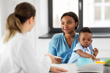 medicine, healthcare and pediatry concept - caucasian doctor giving prescription to african american mother with baby son at clinic - Powered by Adobe