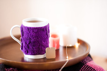 Fototapeta na wymiar Knitted cup of tea with candles at background closeup. Winter season.
