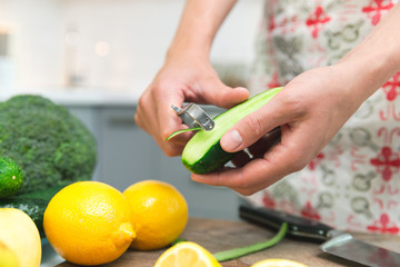 Woman cooking healthy food in her kitchen, she is peeling a fresh cucumber on the chopping board