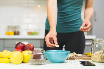 Woman preparing healthy fitness breakfast: oatmeal with bananas, strawberries and chia seeds