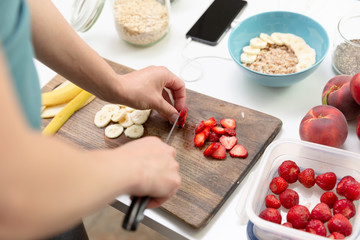 Obraz na płótnie Canvas Woman preparing healthy fitness breakfast: oatmeal with bananas, strawberries and chia seeds