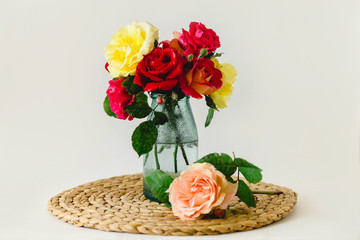 Obraz premium Stunning composition of colorful roses in a glass vase on a wicker napkin