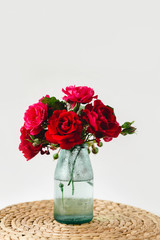 Stunning composition of colorful roses in a glass vase on a wicker napkin