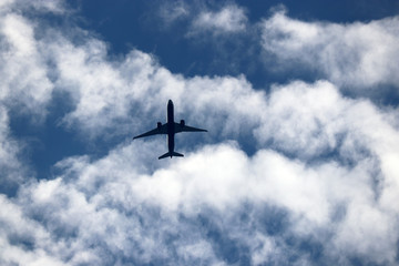 Airplane flying in the blue sky on background of white clouds. Silhouette of a commercial plane during the turn, turbulence concept