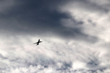 Naklejka na ściany i meble Airplane flying in the sky on background of white and dark clouds. Silhouette of a commercial plane during the turn, turbulence concept