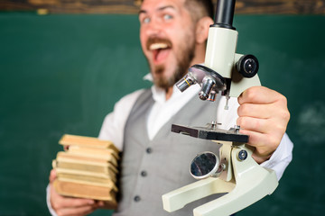Scientist, docent, student with books and microscope in auditorium. Happy male teacher with books and microscope. Education, research, knowledge, technology. Student holds microscope. Selective focus.