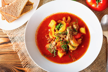 Hot beef hungarian  goulash soup with paprika, beef, potatoes, carrots, onion, pepper and herbs. Ingredients for dish.  Rustic background.