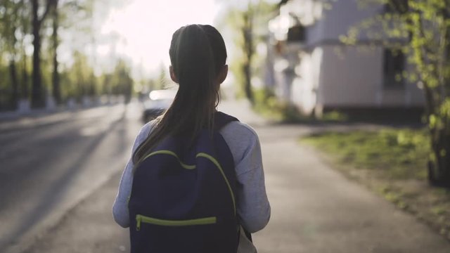 Child girl is walking with a school bag in sunny day. Steadicam shot, front view, 4K
