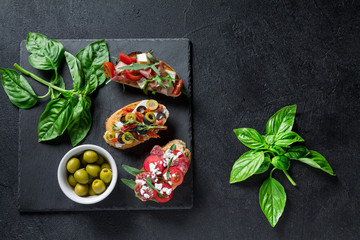 Three bruschetta on a black square slate dish on a dark background. Top view with copy space for your text