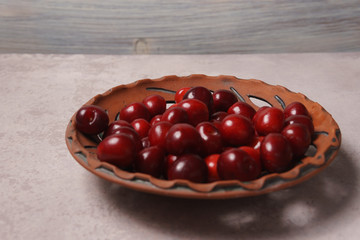 Red sweet cherry in a clay plate on a cream table