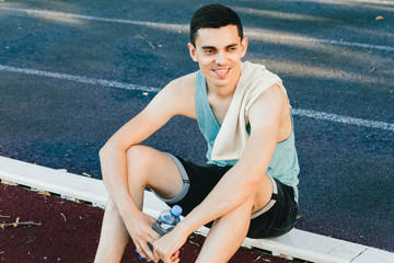 Young man sitting on the ground with a bottle of water after Jogging outdoors