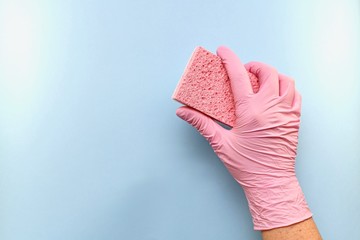 Pink household sponge made of natural scourer, abrasive side down, in the right hand  and in a pink rubber glove. On a blue background on the right in the center keeps it tilted.