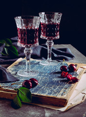Two glasses with cherry liqueur and cherry berries on the background of an old, shabby book. Embedded Still Life