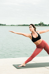 young girl doing yoga outdoors on the pier by the lake.
