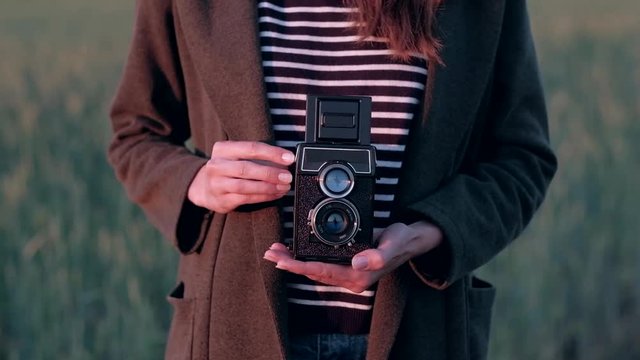 Hands of girl stands in field holding vintage camera. Woman photographer take a photo on hasselblad. 