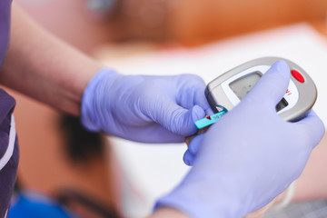 Nurse holding a blood glucose monitoring system while checking the results on it – Diabetes meter in hands of a person wearing blue sterile surgical gloves