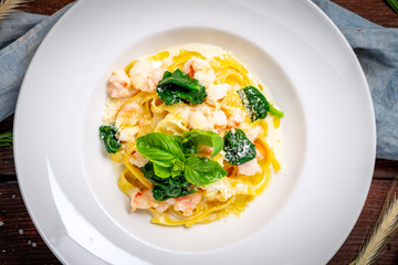 Tagliatelle with seafood. Traditional Italian pasta with shrimp, Basil in cream sauce on a white plate. Top view, close up