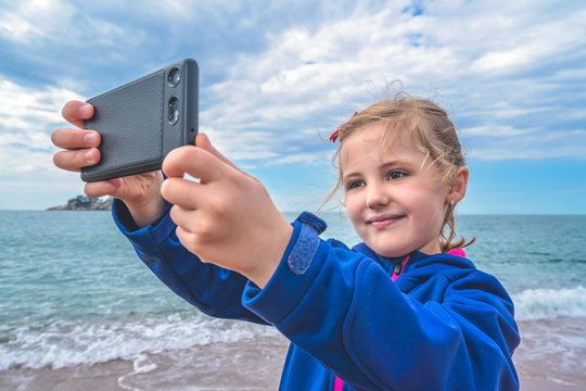 Cute little girl taking selfie on the beach