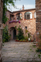 Montemerano, Grosseto, Tuscany. Public square of the medieval town. Stone paving and red brick walls. Arch with stairs adorned with flowers