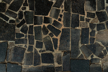 The texture of the sidewalk of chaotic granite stones of different colors with many cracks