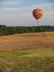 Hot air balloon floats over golden farm field