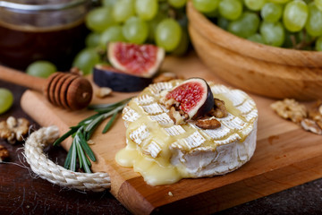 Baked Camembert on wooden board, grapes, figs, nuts, honey, herbs - obrazy, fototapety, plakaty