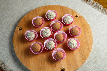 Homemade candy in the form of balls of dried fruit with walnut and cocoa powder on a wooden plank on a linen napkin on the table. Healthy food without sugar and gluten.