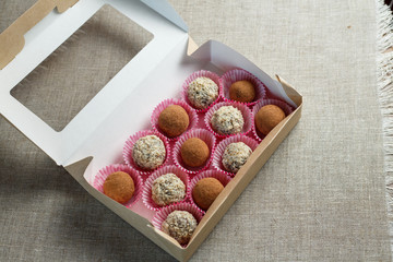 Obraz premium Homemade candy in the form of balls of dried fruit with walnut and cocoa powder in the box on a linen napkin on the table. Healthy food without sugar and gluten.