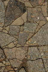 The texture of the sidewalk of chaotic granite stones of different colors with many cracks